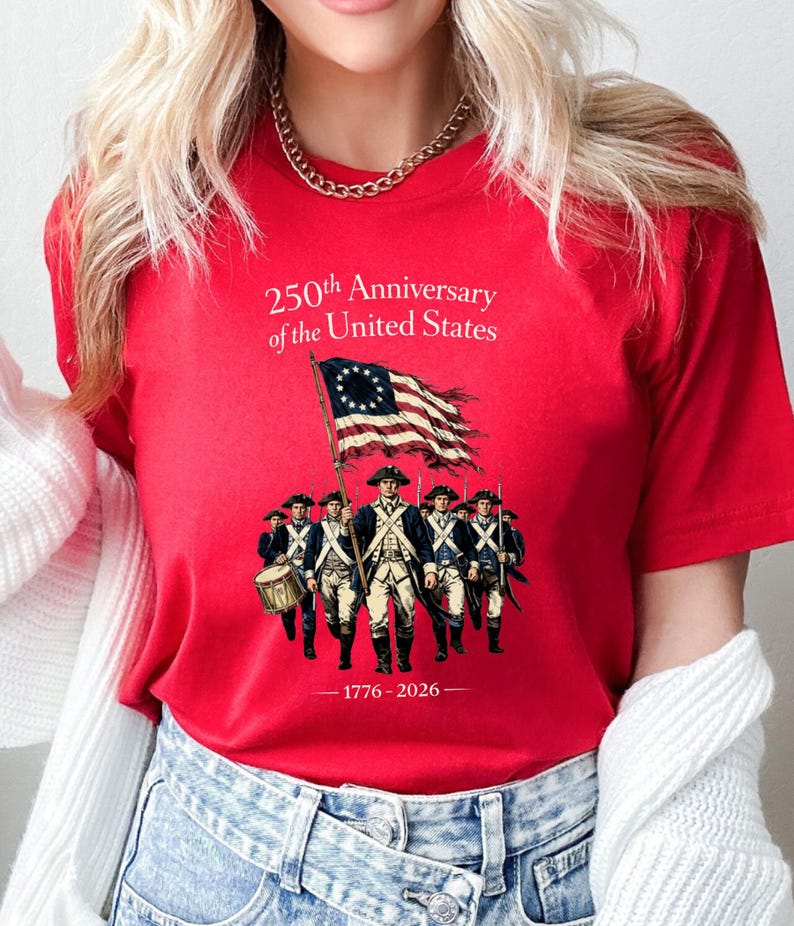 May include: Red t-shirt featuring a graphic commemorating the 250th Anniversary of the United States. The design includes an illustration of soldiers, a flag, and the years 1776-2026.