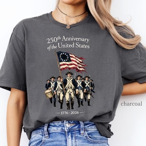 May include: Charcoal-colored t-shirt featuring a graphic commemorating the 250th anniversary of the United States. The design includes an illustration of soldiers, a flag, and the text "250th Anniversary of the United States" and "1776-2026".
