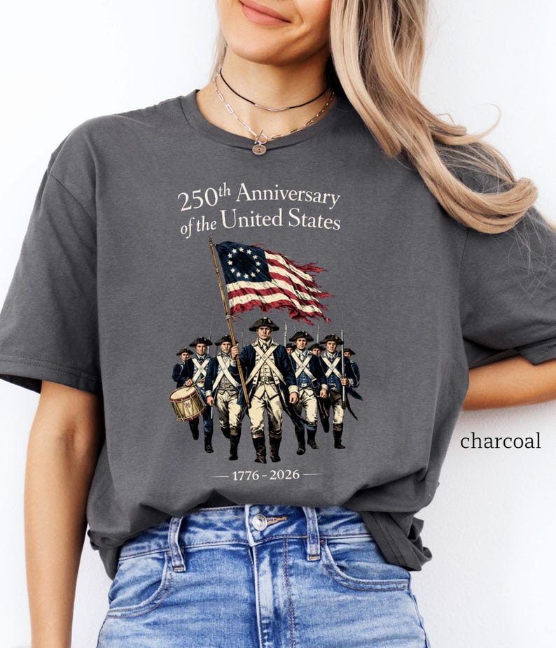 May include: Charcoal-colored t-shirt featuring a graphic commemorating the 250th anniversary of the United States. The design includes an illustration of soldiers, a flag, and the text "250th Anniversary of the United States" and "1776-2026".