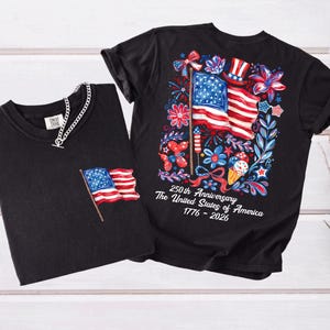 May include: Two black t-shirts. One has a small American flag on the pocket. The other has a large graphic of the American flag, fireworks, and flowers, with the text "250th Anniversary The United States of America 1776-2026."