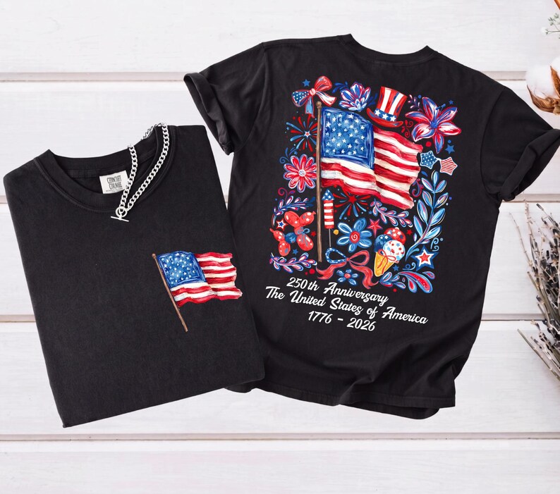 May include: Two black t-shirts. One has a small American flag on the pocket. The other has a large graphic of the American flag, fireworks, and flowers, with the text "250th Anniversary The United States of America 1776-2026."
