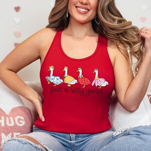 K&ouml;nnte beinhalten: Rotes Tanktop mit vier Cartoon-G&auml;nsen in verschiedenen Outfits. Unter den G&auml;nsen steht der Text "just a silly goose". Die G&auml;nse tragen ein Kleid, eine Jacke, ein Erdbeerkost&uuml;m und einen Rock.