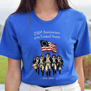 May include: Royal blue t-shirt featuring a graphic commemorating the 250th anniversary of the United States. The design includes an illustration of soldiers, a flag, and the years 1776-2026.