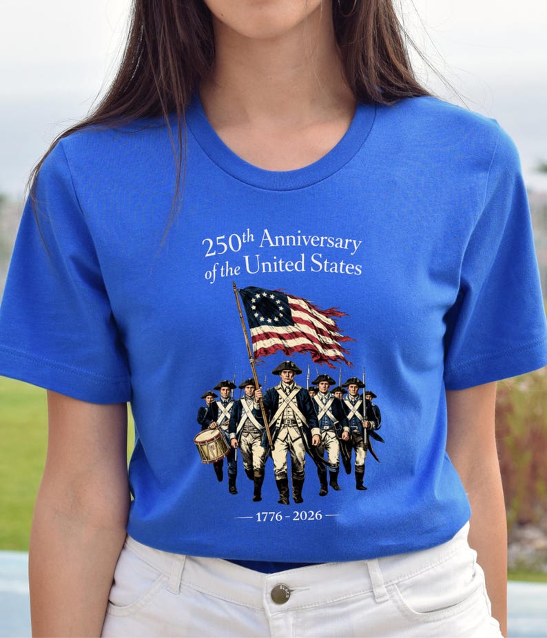 May include: Royal blue t-shirt featuring a graphic commemorating the 250th anniversary of the United States. The design includes an illustration of soldiers, a flag, and the years 1776-2026.