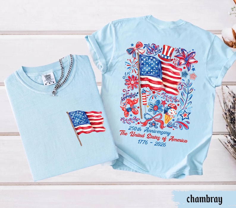 May include: Two light blue t-shirts. One has a small American flag on the pocket. The other has a large graphic of the American flag, fireworks, and text that reads "250th Anniversary The United States of America 1776-2026."
