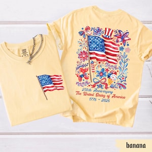 May include: Two light yellow t-shirts. One has a small American flag graphic on the pocket. The other has a large American flag design on the back, surrounded by floral and celebratory elements. Text reads "250th Anniversary The United States of America 1776-2026."