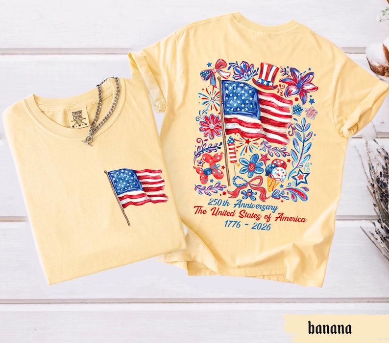 May include: Two light yellow t-shirts. One has a small American flag graphic on the pocket. The other has a large American flag design on the back, surrounded by floral and celebratory elements. Text reads "250th Anniversary The United States of America 1776-2026."