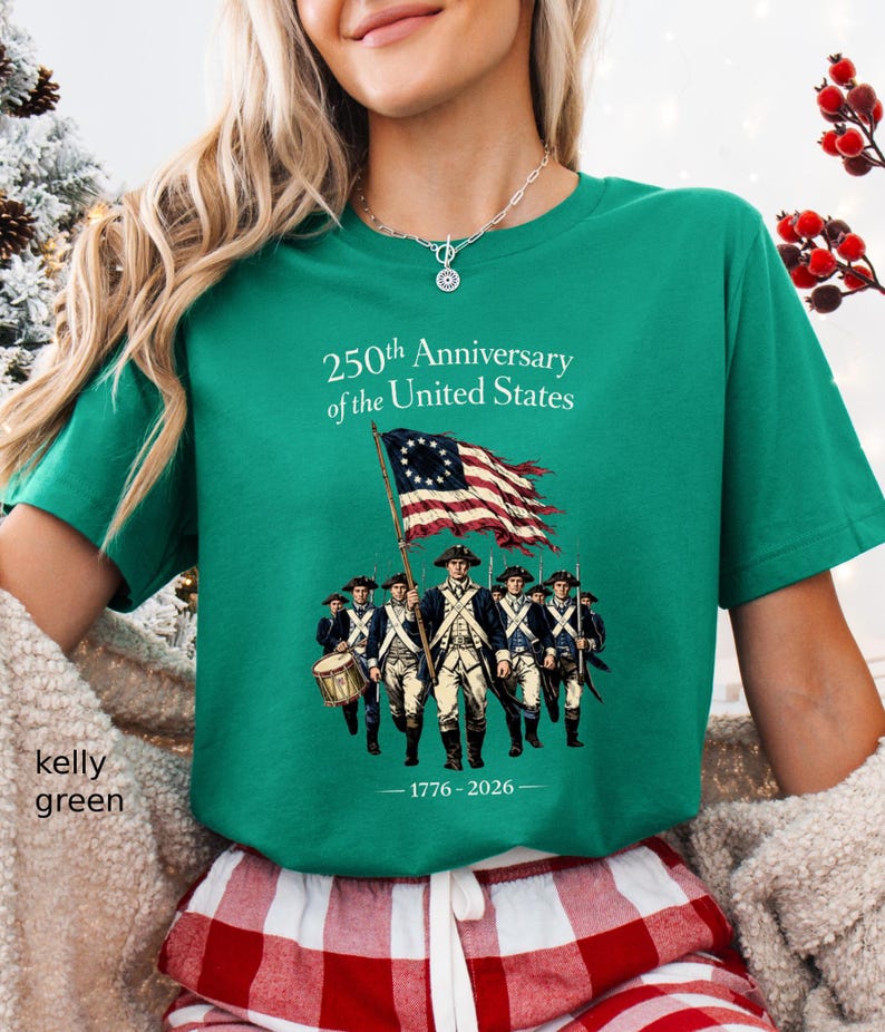 May include: Kelly green t-shirt with the text "250th Anniversary of the United States" and an illustration of soldiers and a flag. The flag has a circle of stars and red and white stripes. The shirt also has the dates 1776-2026.