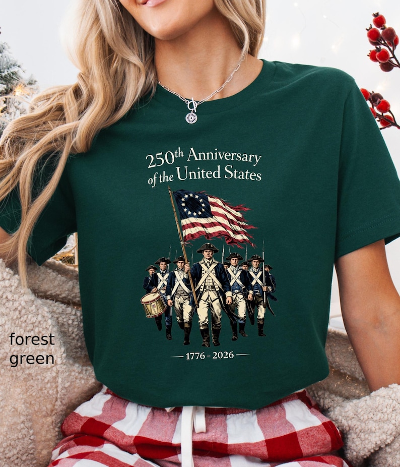 May include: Forest green t-shirt with a graphic commemorating the 250th Anniversary of the United States. The design features a colonial flag and soldiers, with the years 1776-2026. The text "250th Anniversary of the United States" is printed above the graphic.
