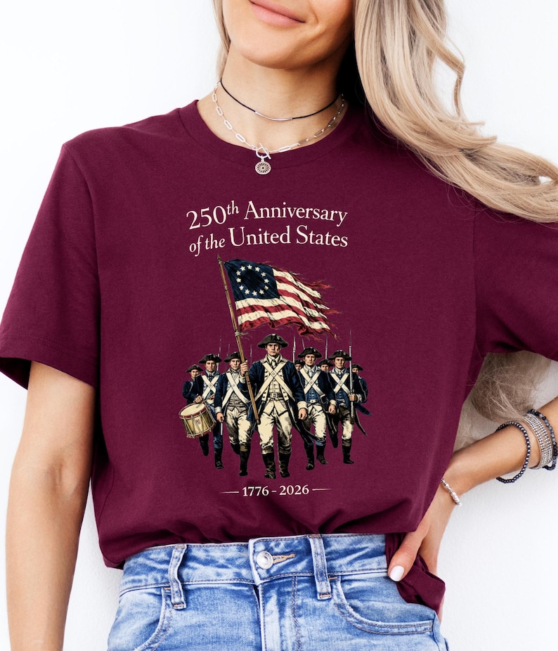 May include: Burgundy t-shirt featuring a graphic commemorating the 250th anniversary of the United States. The design includes an illustration of soldiers marching with a flag, and the years 1776-2026.