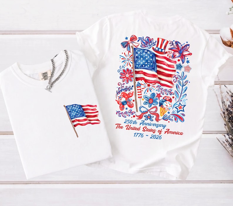 May include: Two white t-shirts with patriotic designs. One shirt features a small American flag graphic, and the other displays a larger flag design with floral and firework elements. Text on the shirt reads "250th Anniversary The United States of America 1776-2026."