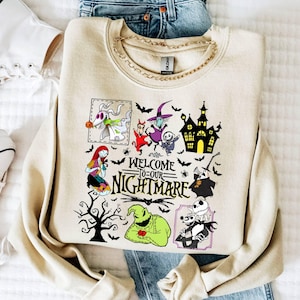 May include: A beige crewneck sweatshirt featuring a graphic print with the text "WELCOME TO OUR NIGHTMARE" surrounded by various animated characters, a haunted house, a bare tree, and bats. The design includes colorful illustrations.