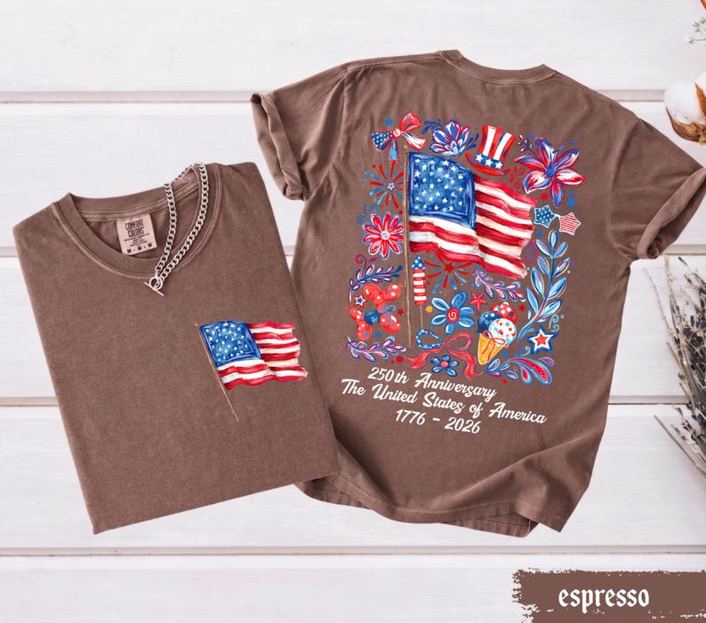 May include: Two espresso-colored t-shirts. One has a small American flag on the pocket. The other has a large graphic of the American flag with floral and firework designs. Text on the back reads "250th Anniversary The United States of America 1776-2026."