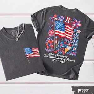May include: Two dark gray t-shirts with American flag designs. One shirt has a small flag on the pocket, and the other has a large flag design on the back with the text "250th Anniversary The United States of America 1776-2026".