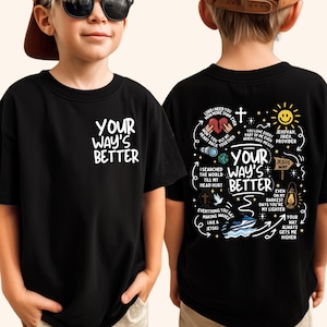 May include: Black t-shirt with the text "YOUR WAY'S BETTER" in white on the front. The back of the shirt features a graphic design with religious themes, including a cross, sun, and various phrases. The shirt is worn by a child.