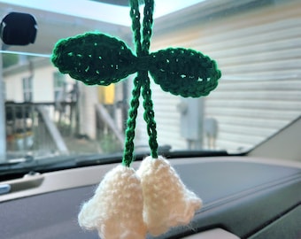 May include: A white crocheted flower with green leaves hanging from a rearview mirror in a car.