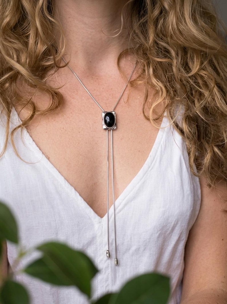 Woman wearing silver bolo tie necklace with black onyx over a blouse, showcasing elegant Y shape drape and minimalist western style suitable for both casual and dressy outfits.