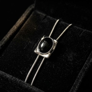 Silver bolo tie necklace with black onyx stone centerpiece displayed on a dark background, featuring a minimalist Y chain design, adjustable length, and sleek modern western style, perfect for women’s everyday jewelry or cowboy-inspired outfits.