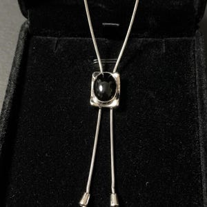 Close-up of black onyx stone reflecting light with deep glossy finish, set in a geometric silver frame, emphasizing modern luxury and understated western jewelry aesthetic.