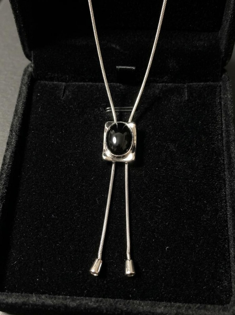 Close-up of black onyx stone reflecting light with deep glossy finish, set in a geometric silver frame, emphasizing modern luxury and understated western jewelry aesthetic.