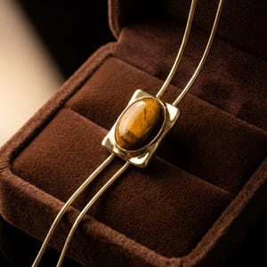 Women’s western bolo tie necklace displayed as vintage inspired jewelry combining minimalist gold chain and tiger eye pendant.