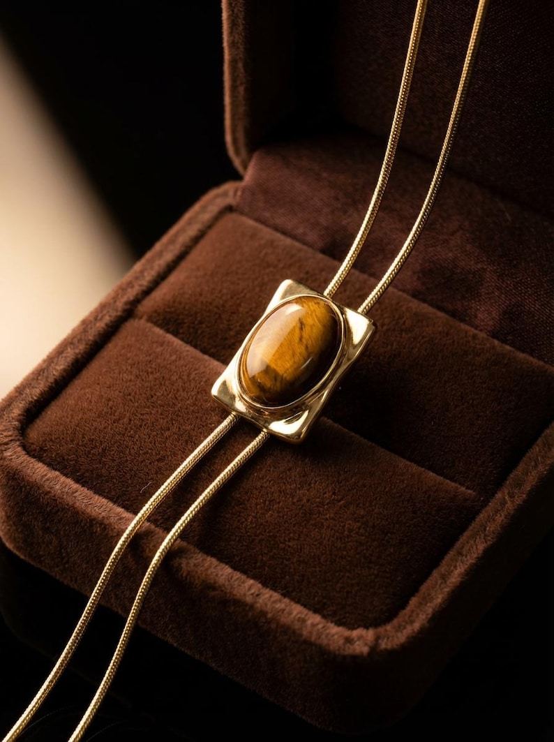 Women’s western bolo tie necklace displayed as vintage inspired jewelry combining minimalist gold chain and tiger eye pendant.