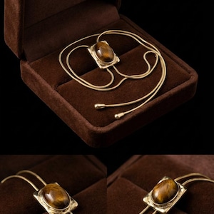 Women’s western bolo tie necklace displayed as vintage inspired jewelry combining minimalist gold chain and tiger eye pendant.