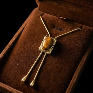Close-up of the tiger eye gemstone showing warm brown and golden patterns inside a minimalist gold pendant frame.