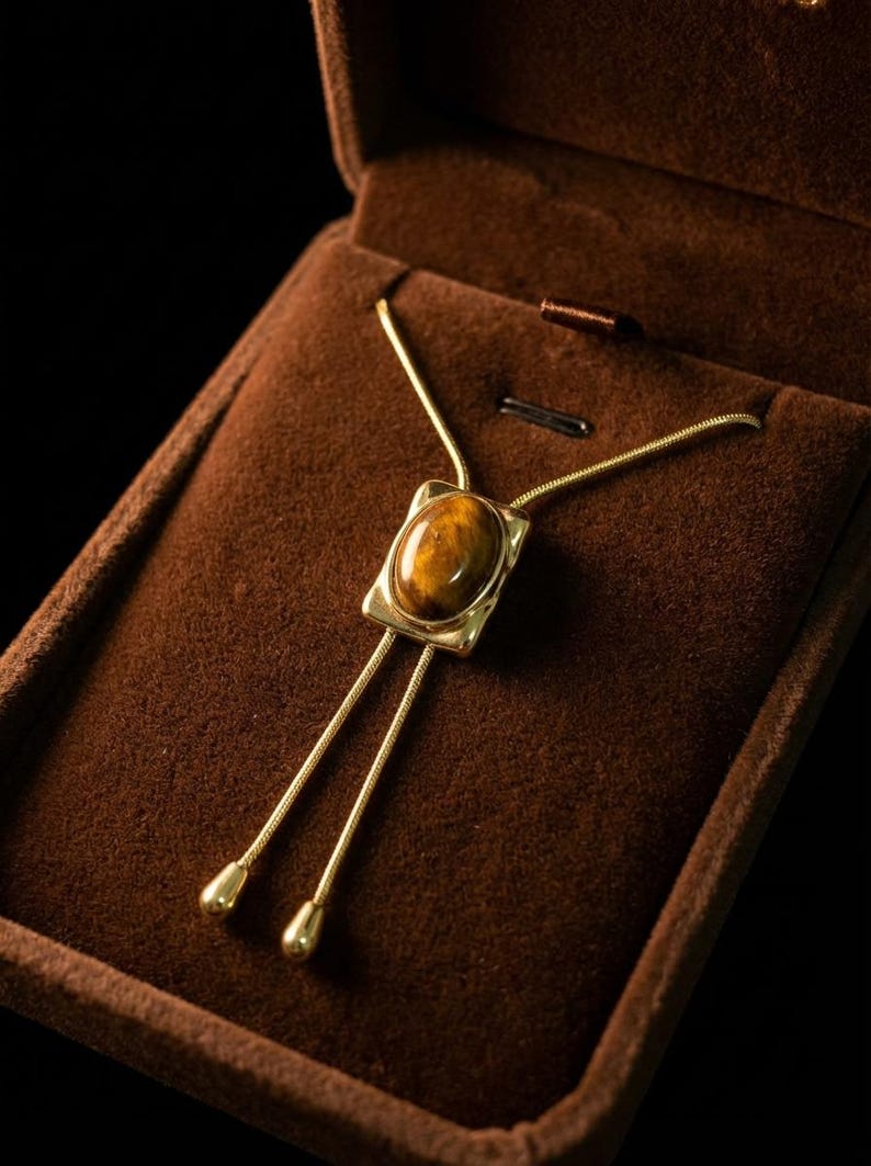 Close-up of the tiger eye gemstone showing warm brown and golden patterns inside a minimalist gold pendant frame.