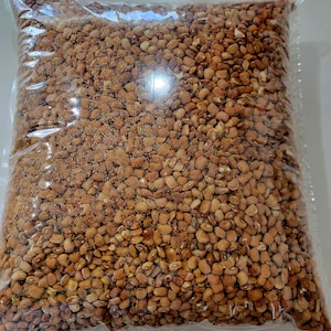 May include: A clear plastic bag filled with brown beans. The beans are a light brown color and have a slightly rough texture.