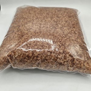 May include: A clear plastic bag filled with brown rice. The rice is loose and uncooked.