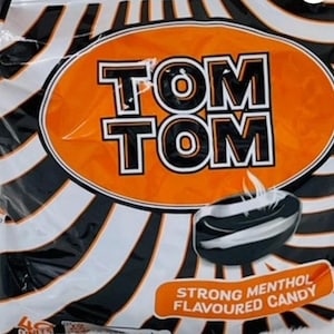 May include: A bag of Tom Tom strong menthol flavored candy. The bag is black and white with an orange circle in the center that says "Tom Tom" in black letters. The candy is black and white and looks like a round disc.