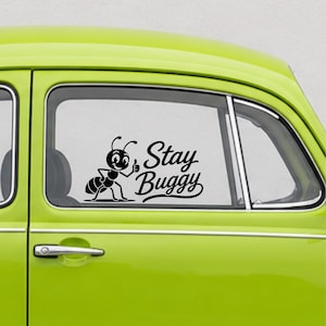 May include: A black vinyl decal applied to the window of a lime green car. The decal features a cartoon ant giving a thumbs up next to the text Stay Buggy written in a cursive script font. The design is positioned on the glass surface.