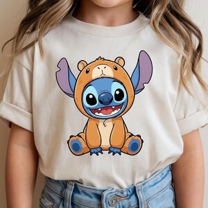 A person wearing a white t-shirt with a cartoon character of a smiling, cartoon-like creature with large ears and a blue body.