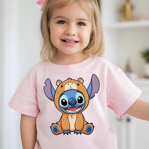A young girl wearing a pink t-shirt with a cartoon character printed on it.
