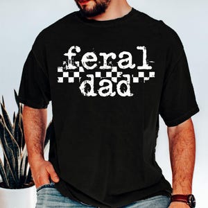 A man wearing a black t-shirt with the text "feral dad" printed on it.