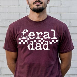 A man wearing a maroon t-shirt with the text "feral dad" printed on it.