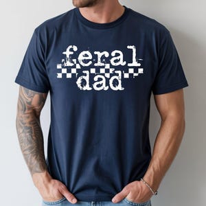 A man wearing a navy blue t-shirt with the text "feral dad" printed on it.