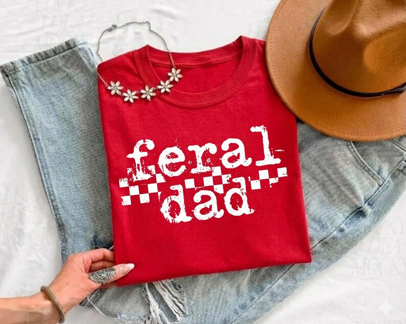 A red t-shirt with the text "feral dad" printed on it, along with a brown hat and a necklace.
