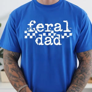 A person wearing a blue t-shirt with the text "feral dad" printed on it.