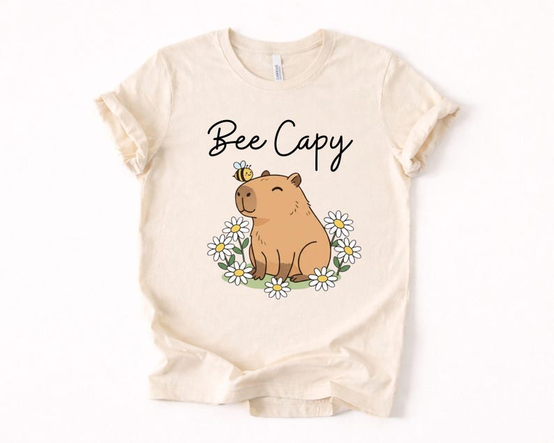 A white t-shirt with a cartoon image of a capybara surrounded by flowers and a bee.
