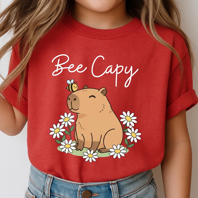 A red t-shirt with a cartoon image of a capybara surrounded by flowers and a bee.