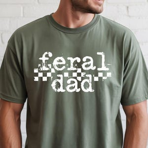 A man wearing a green t-shirt with the text "feral dad" printed on it.
