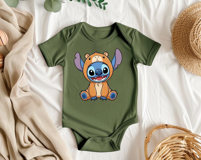 A green baby onesie with a cartoon character design is displayed on a bed, surrounded by various clothing items and accessories.