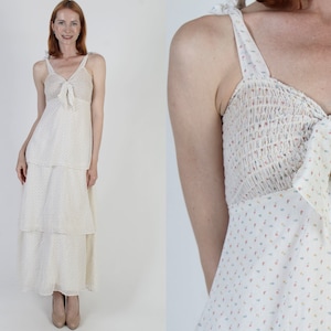 May include: A white tiered maxi dress with a floral print and a tie at the bust. The dress has thin straps and a relaxed fit.