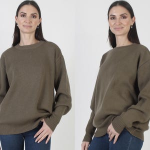 Puede incluir: Un su&eacute;ter verde oliva con cuello redondo y pu&ntilde;os y dobladillo acanalados. El su&eacute;ter est&aacute; hecho de un material de punto suave y se usa con jeans azules. El su&eacute;ter tiene mangas largas y un ajuste holgado.