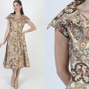 May include: A vintage-style dress featuring a paisley pattern in beige, brown, and muted red tones. The dress has a V-neckline, short sleeves, and a flared skirt. The dress is knee-length and appears to be made of a lightweight fabric.