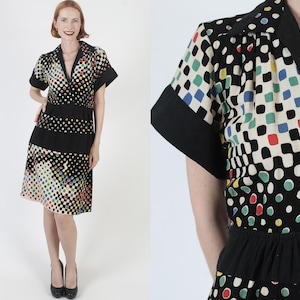 May include: A black and white dress with a colorful geometric pattern. The dress has a collared neckline, short sleeves, and a fitted bodice. The skirt is full and falls to the knees.