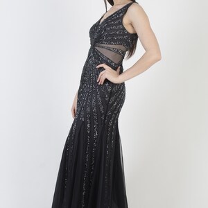 May include: A sleeveless black evening gown with a V-neckline and a flowing skirt. The dress is embellished with vertical rows of silver sequins. The bodice features a sheer panel at the waist. The gown is floor-length and suitable for formal events.