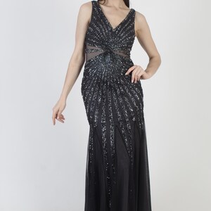 May include: A sleeveless black evening gown with a V-neckline and a flowing skirt. The bodice features intricate sequin detailing in a radiating pattern. A sheer panel is visible at the waist, adding a touch of elegance to the formal dress.
